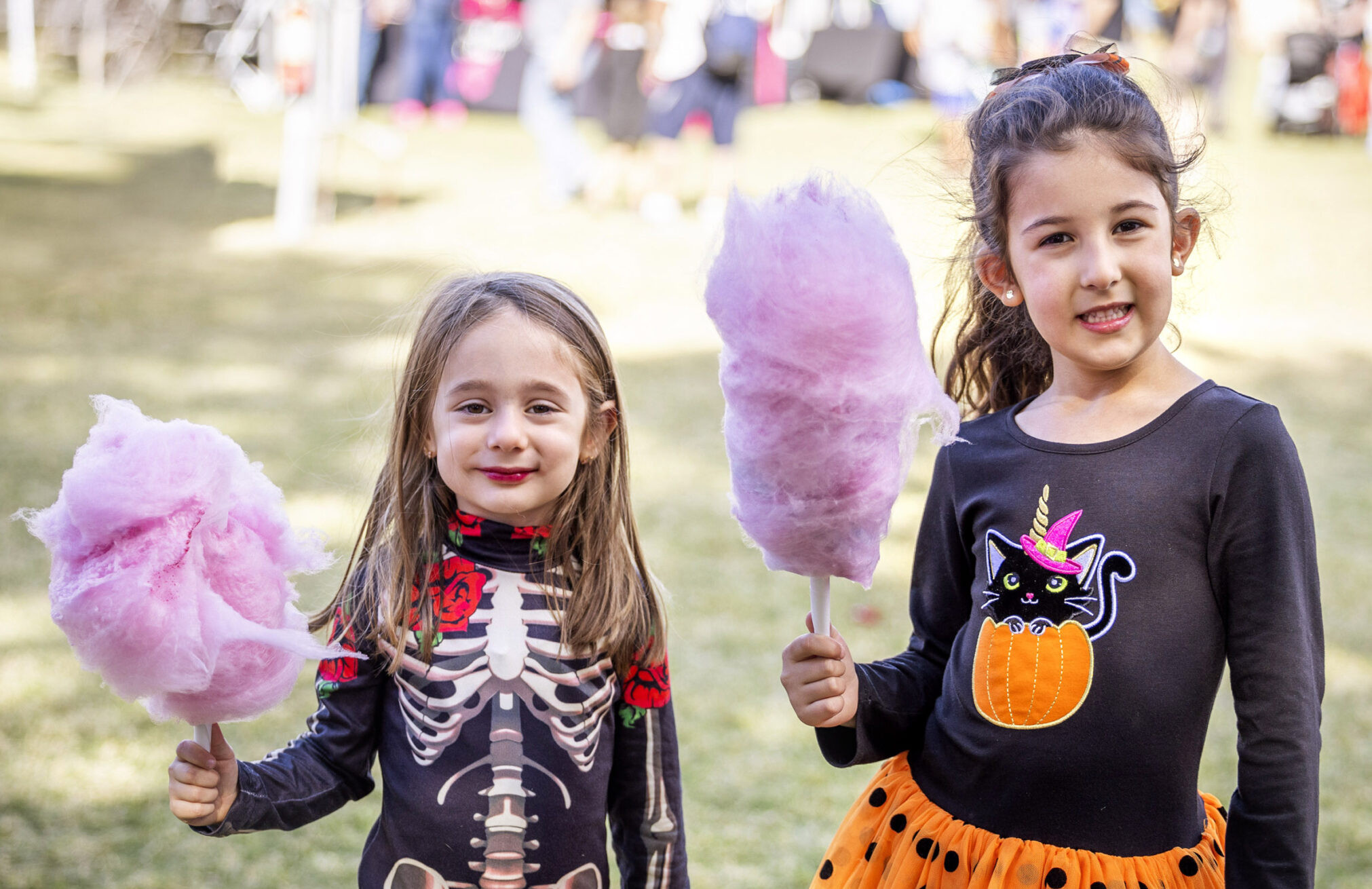 Two young girls in Halloween costumes holding cotton candy at an outdoor event.