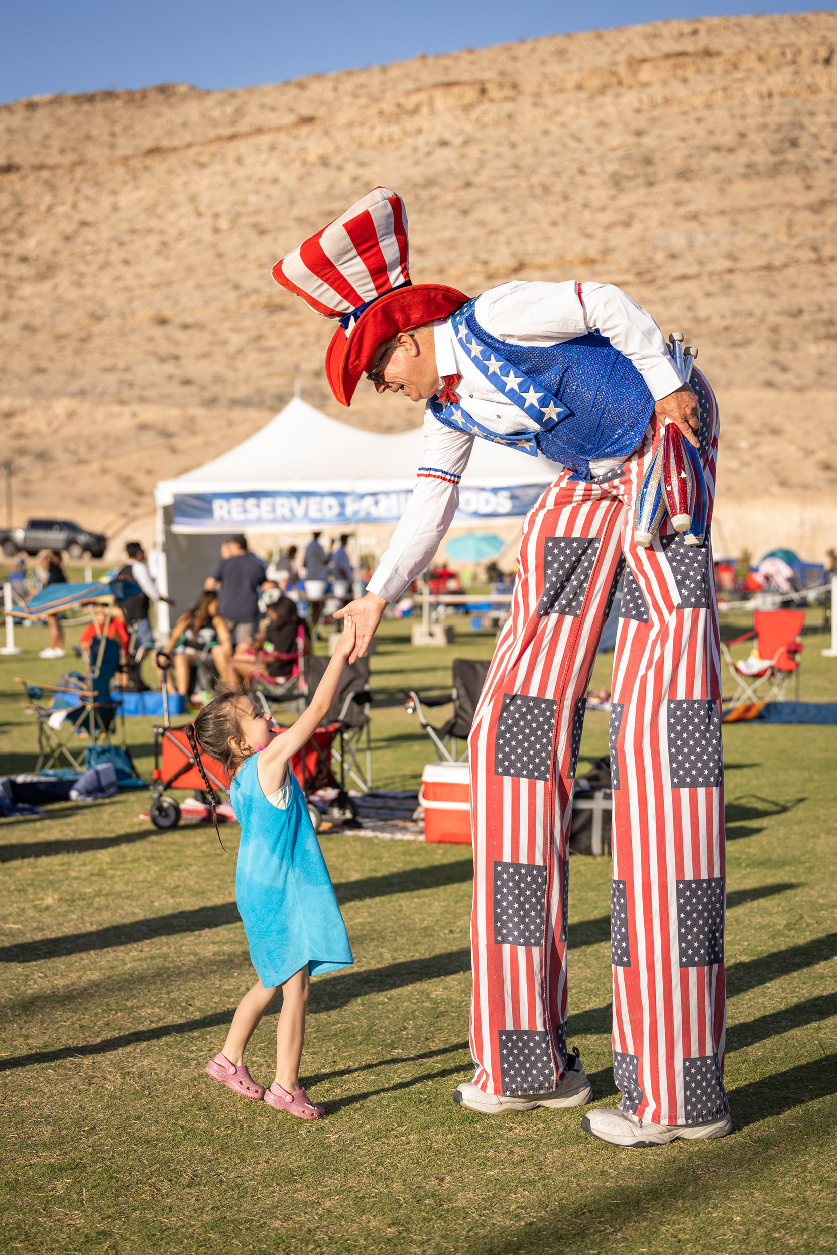 Uncle Sam on stilts interacts with a young girl at an outdoor patriotic event.