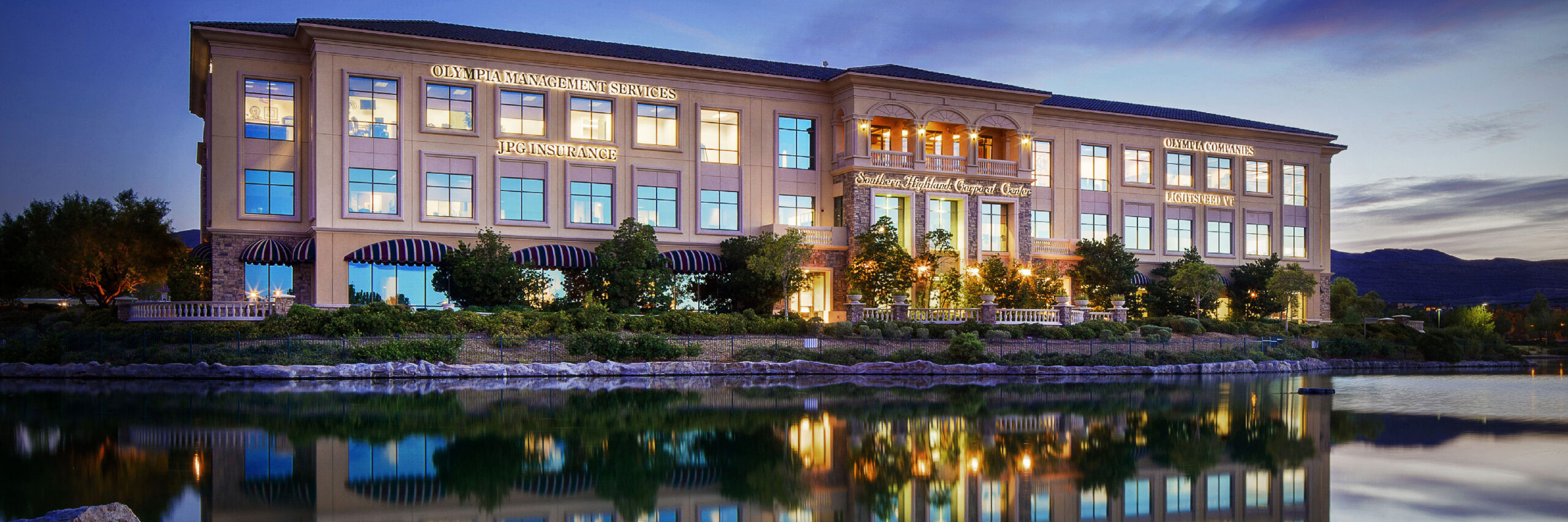 Community and property management services building at dusk with reflection in water.